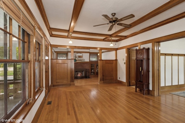 empty room featuring visible vents, a wood stove, wood finished floors, coffered ceiling, and beamed ceiling