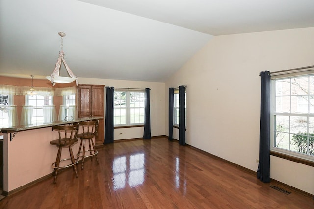 kitchen featuring dark wood-style flooring, visible vents, brown cabinets, a kitchen bar, and lofted ceiling