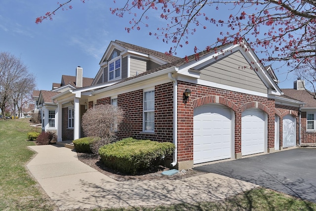 view of property exterior with a chimney, a garage, driveway, and brick siding