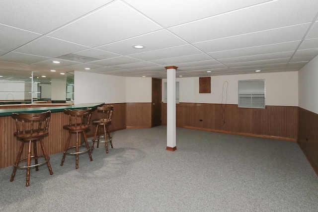 bar featuring carpet, a drop ceiling, a wainscoted wall, a bar, and wood walls