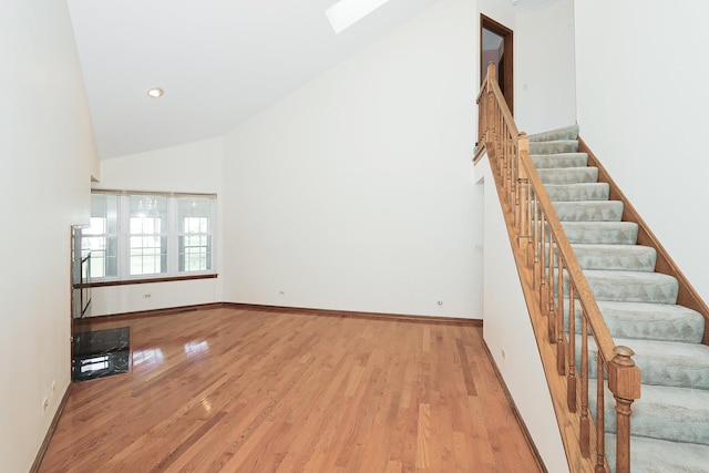 unfurnished living room featuring high vaulted ceiling, a skylight, wood finished floors, stairs, and baseboards