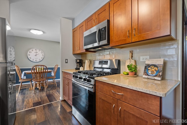 kitchen with light stone counters, dark wood-style floors, stainless steel appliances, brown cabinetry, and decorative backsplash