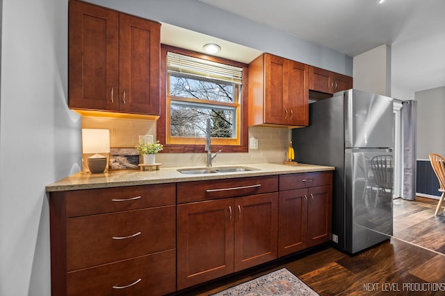 kitchen featuring a sink, backsplash, dark wood-style floors, freestanding refrigerator, and light stone countertops