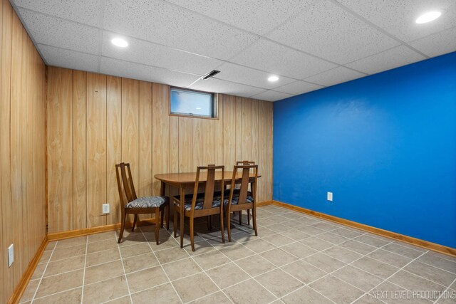 dining room with visible vents, baseboards, a paneled ceiling, and wooden walls