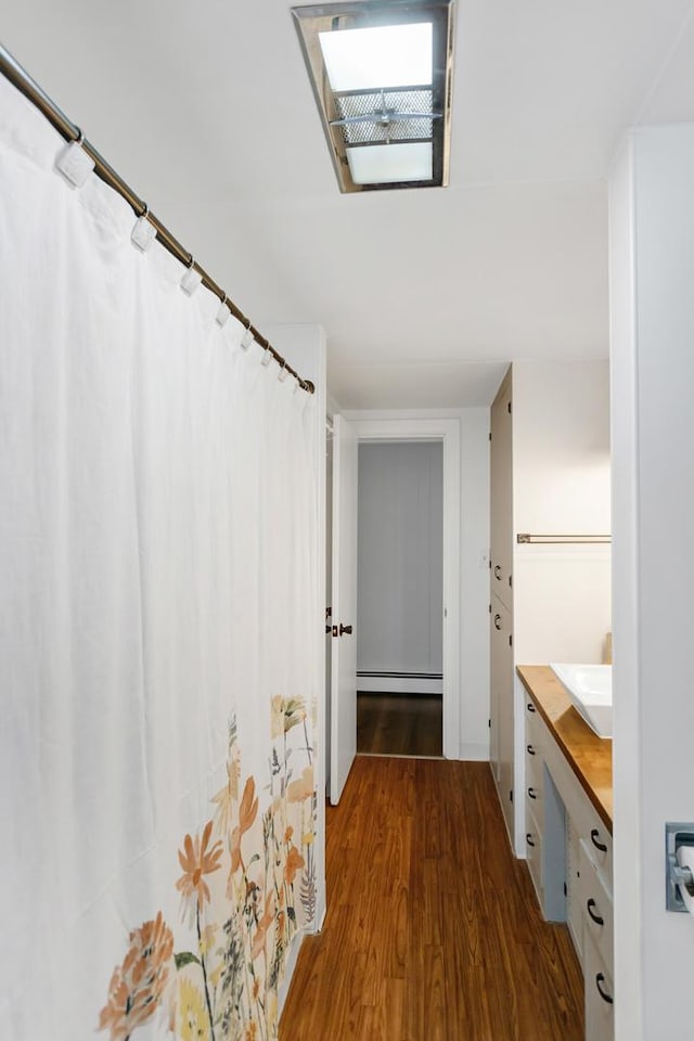 full bath with curtained shower, a baseboard radiator, wood finished floors, and vanity