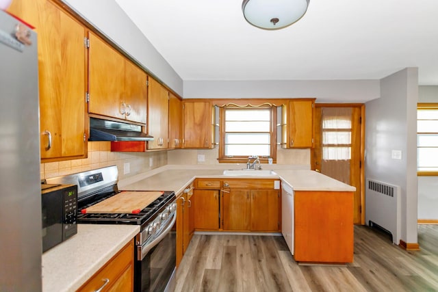 kitchen featuring radiator heating unit, appliances with stainless steel finishes, light countertops, under cabinet range hood, and a sink