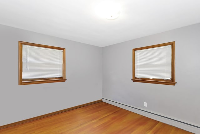 unfurnished room featuring a baseboard heating unit, light wood-style flooring, and baseboards