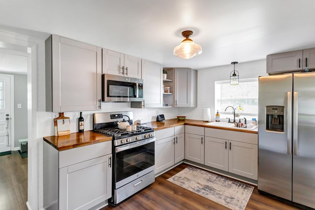 kitchen with stainless steel appliances, a sink, wood counters, tasteful backsplash, and dark wood finished floors