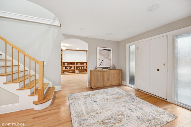 foyer entrance featuring arched walkways, plenty of natural light, stairway, and wood finished floors