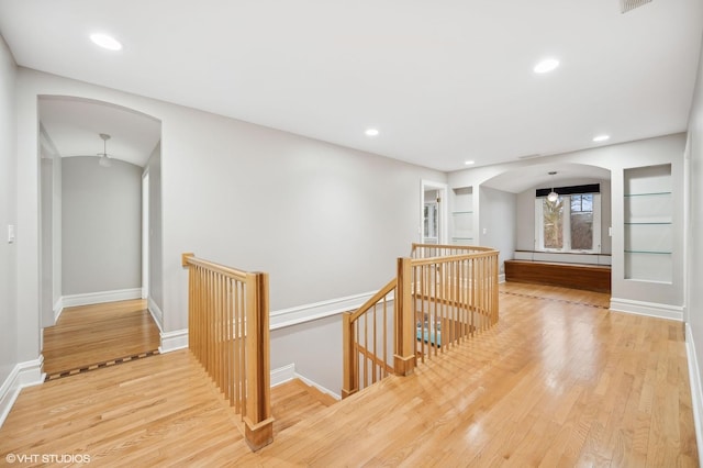 corridor featuring recessed lighting, arched walkways, wood finished floors, and an upstairs landing