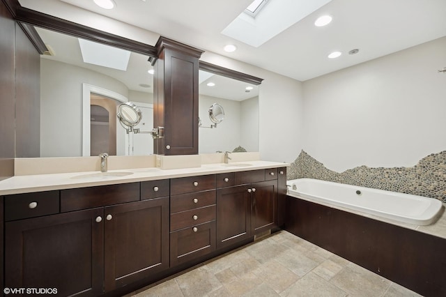 bathroom featuring double vanity, a skylight, a garden tub, and a sink