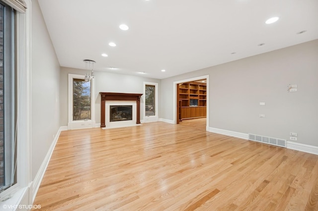 unfurnished living room featuring recessed lighting, visible vents, light wood-style floors, a fireplace with flush hearth, and baseboards