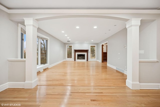 unfurnished living room featuring light wood-style flooring, a fireplace, visible vents, baseboards, and ornate columns