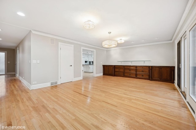 spare room featuring light wood-style floors, baseboards, visible vents, and crown molding