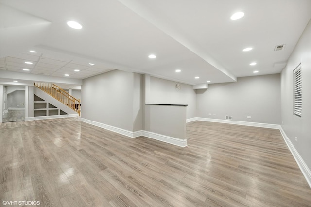 finished below grade area featuring light wood-type flooring, visible vents, baseboards, and stairs