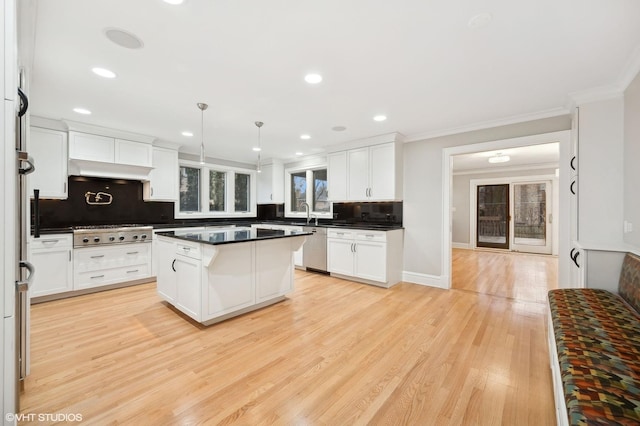 kitchen with appliances with stainless steel finishes, dark countertops, light wood-style flooring, and crown molding