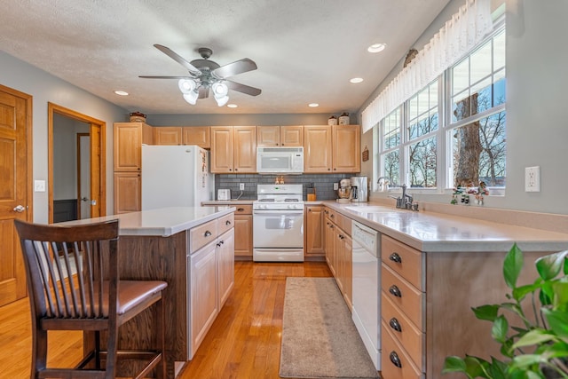 kitchen with white appliances, a breakfast bar area, light countertops, light brown cabinetry, and a sink