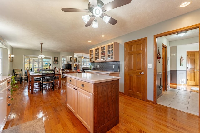 kitchen with glass insert cabinets, a center island, light countertops, and light wood-style flooring