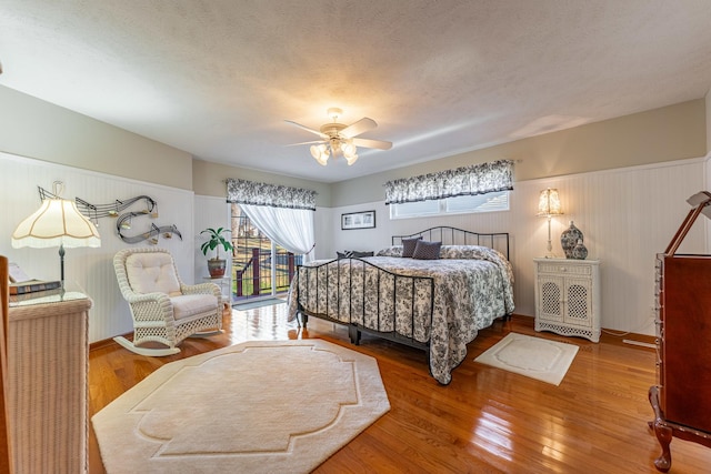 bedroom with ceiling fan, a textured ceiling, hardwood / wood-style flooring, and a wainscoted wall