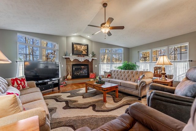 living room with a glass covered fireplace, ceiling fan, wood finished floors, vaulted ceiling, and a textured ceiling