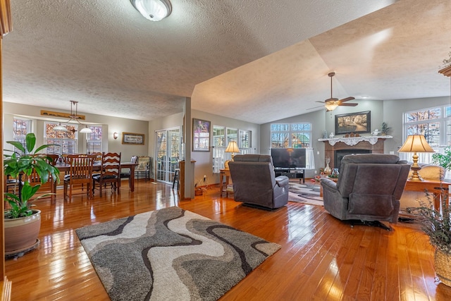 living area featuring a fireplace, lofted ceiling, a ceiling fan, a textured ceiling, and hardwood / wood-style flooring