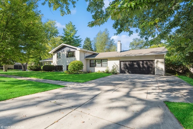 tri-level home with a chimney, stucco siding, a front yard, a garage, and driveway