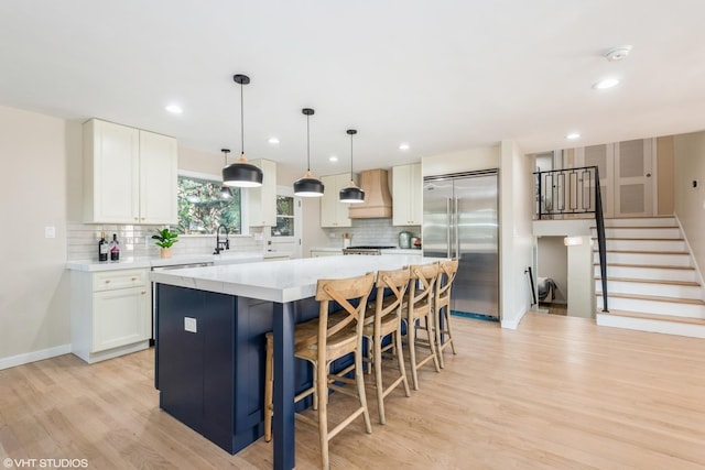 kitchen with decorative backsplash, a kitchen island, stainless steel built in fridge, premium range hood, and white cabinetry