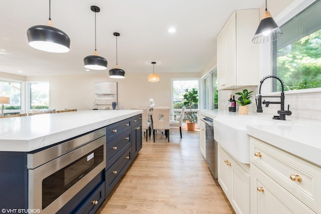 kitchen with light wood finished floors, appliances with stainless steel finishes, white cabinets, and a sink