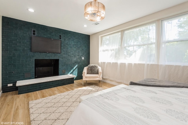 bedroom with a brick fireplace, wood finished floors, visible vents, and recessed lighting