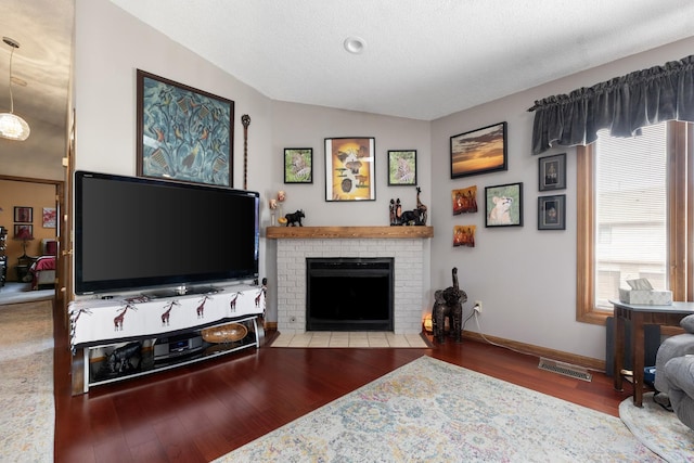 living room featuring lofted ceiling, wood finished floors, visible vents, baseboards, and a brick fireplace