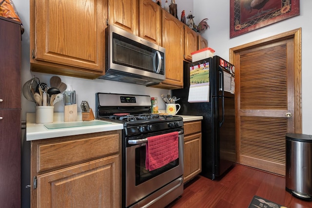 kitchen with stainless steel appliances, brown cabinetry, light countertops, and dark wood finished floors