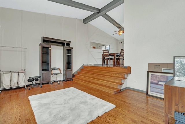 living area featuring baseboards, lofted ceiling with beams, ceiling fan, wood finished floors, and stairs