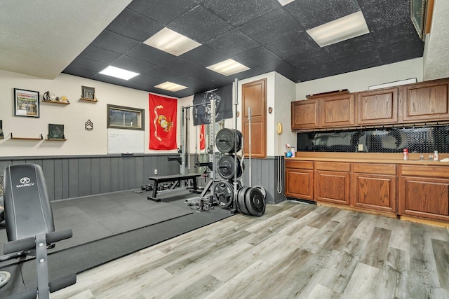 exercise room featuring light wood-type flooring, wainscoting, a sink, and a paneled ceiling