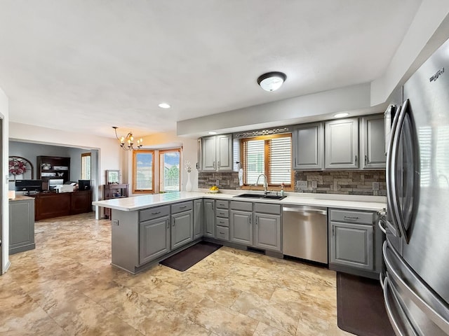 kitchen with a peninsula, a sink, appliances with stainless steel finishes, gray cabinets, and tasteful backsplash