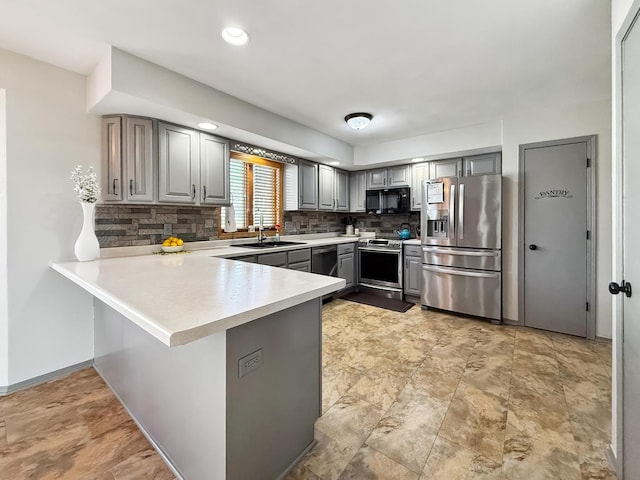 kitchen with a peninsula, light countertops, stainless steel appliances, gray cabinetry, and a sink