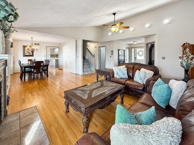 living area with lofted ceiling, stairs, light wood-type flooring, a fireplace, and ceiling fan with notable chandelier