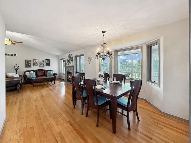 dining area featuring lofted ceiling, light wood-style flooring, visible vents, and a lit fireplace