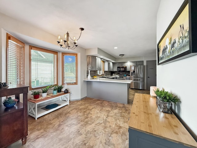 kitchen featuring decorative backsplash, a peninsula, a sink, stainless steel appliances, and a notable chandelier