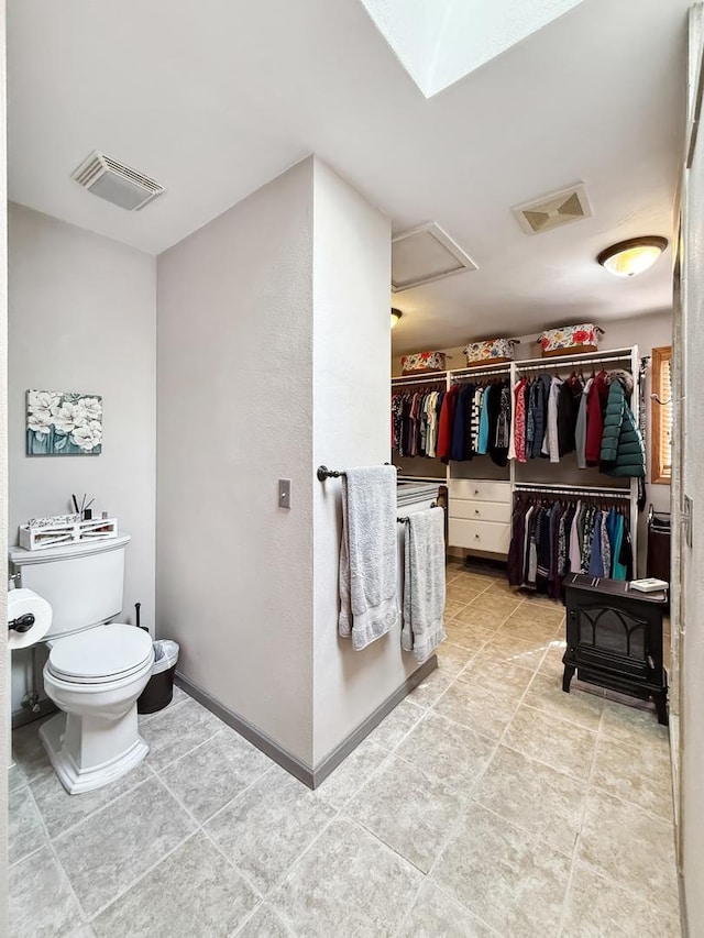 bathroom with baseboards, visible vents, a spacious closet, and toilet