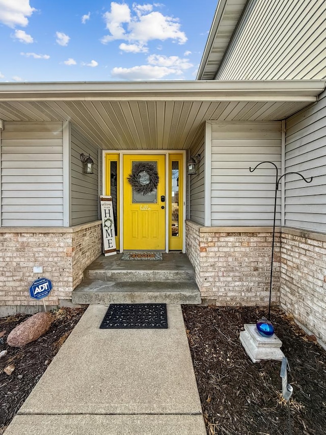 property entrance with a porch and brick siding