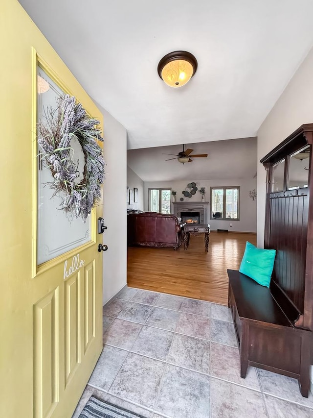 entryway featuring light wood-style floors, a lit fireplace, vaulted ceiling, and a ceiling fan