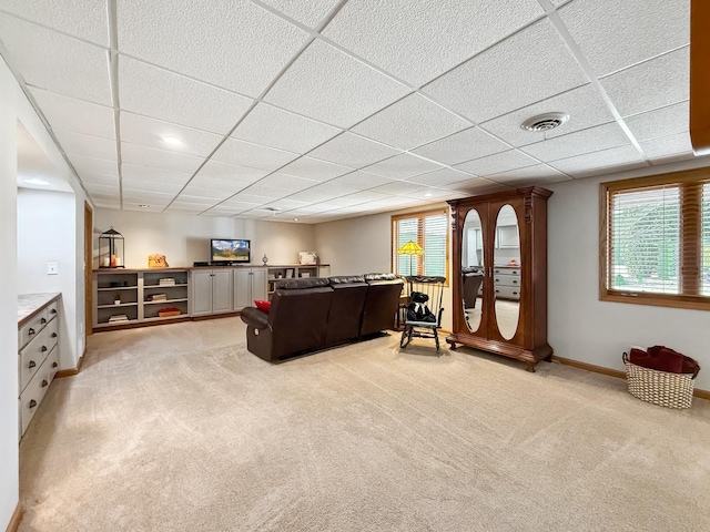 living area with a paneled ceiling, light colored carpet, visible vents, and baseboards