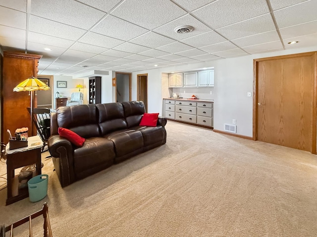 living area with light colored carpet, visible vents, a drop ceiling, and baseboards