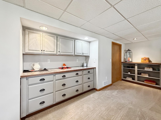 kitchen featuring baseboards, visible vents, light colored carpet, light countertops, and a paneled ceiling