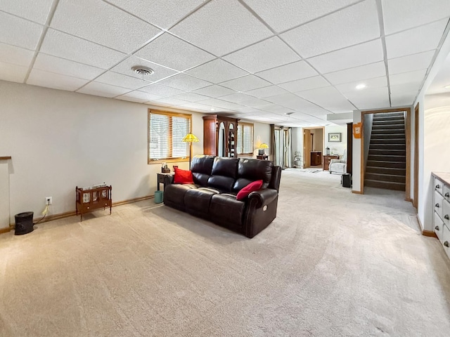 living room featuring light carpet, stairway, a drop ceiling, and baseboards