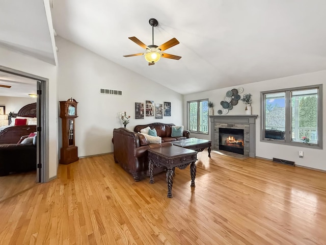 living area featuring visible vents, light wood-style floors, ceiling fan, a stone fireplace, and high vaulted ceiling