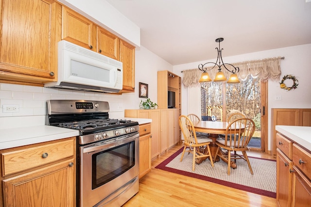 kitchen with light countertops, white microwave, stainless steel range with gas stovetop, and decorative backsplash