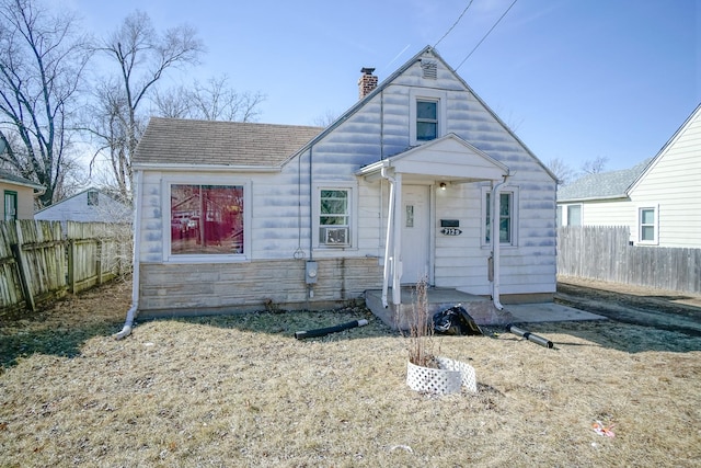 view of front facade with stone siding, a chimney, roof with shingles, and fence