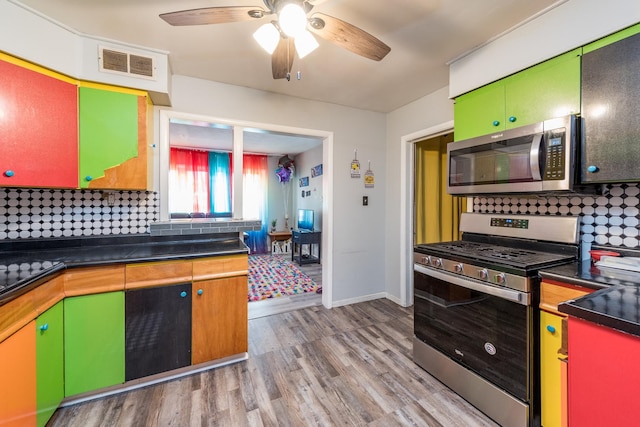 kitchen with light wood finished floors, stainless steel appliances, dark countertops, visible vents, and backsplash