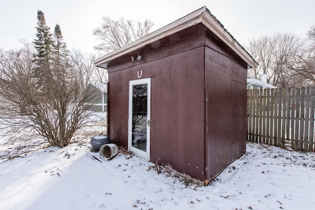 snow covered structure with a storage unit, fence, and an outdoor structure